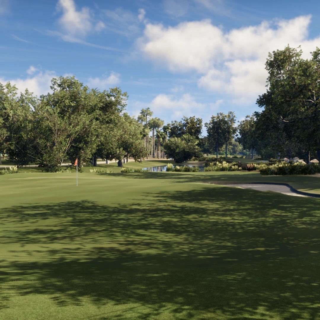 A lush golf course with a green, a hole with a flag, surrounded by trees under a partly cloudy sky.