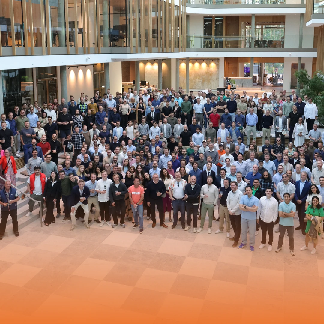 A large group of diverse people gathered in a spacious, modern atrium with glass walls, posing for a group photo.