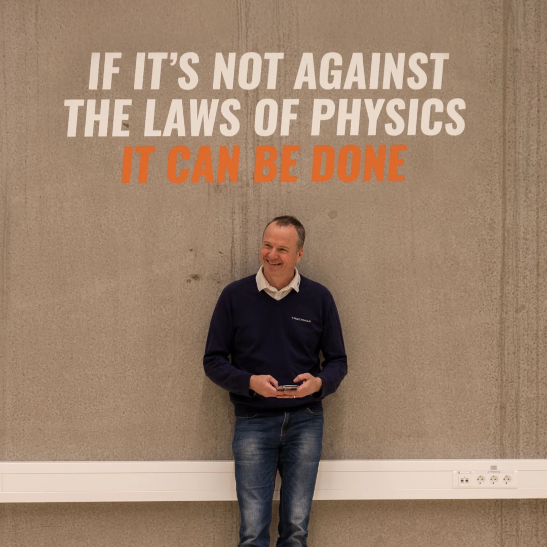 Man smiling in front of a wall with the quote, "If it's not against the laws of physics, it can be done," in bold letters.