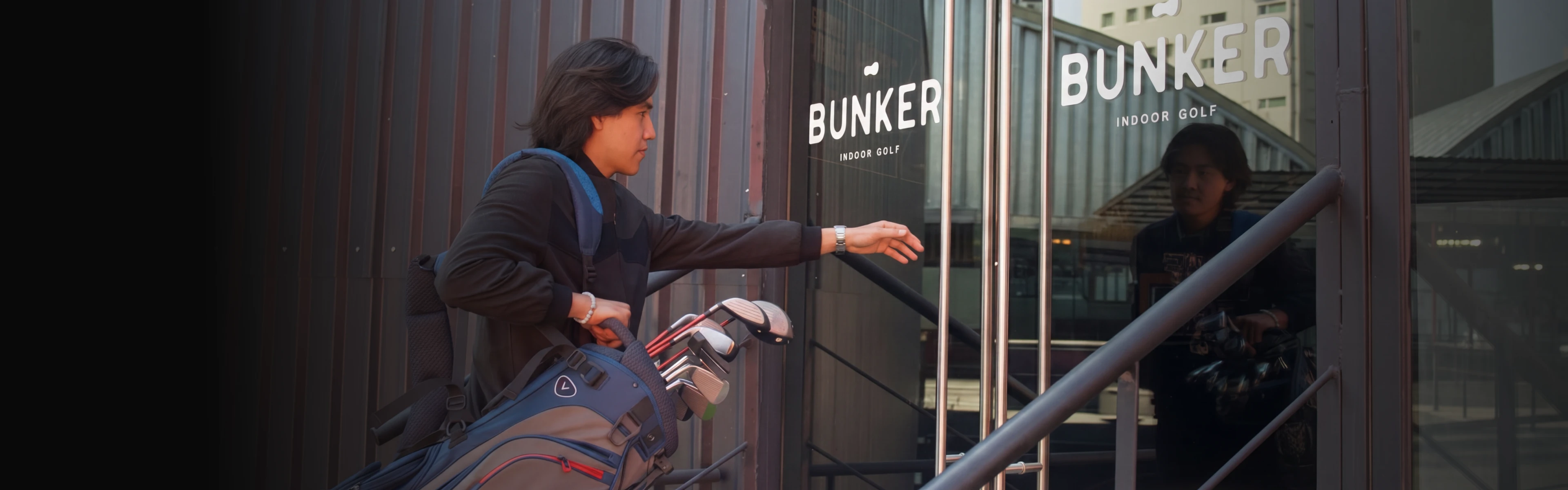 Person entering a building labeled "Bunker Indoor Golf," carrying a golf bag with clubs.