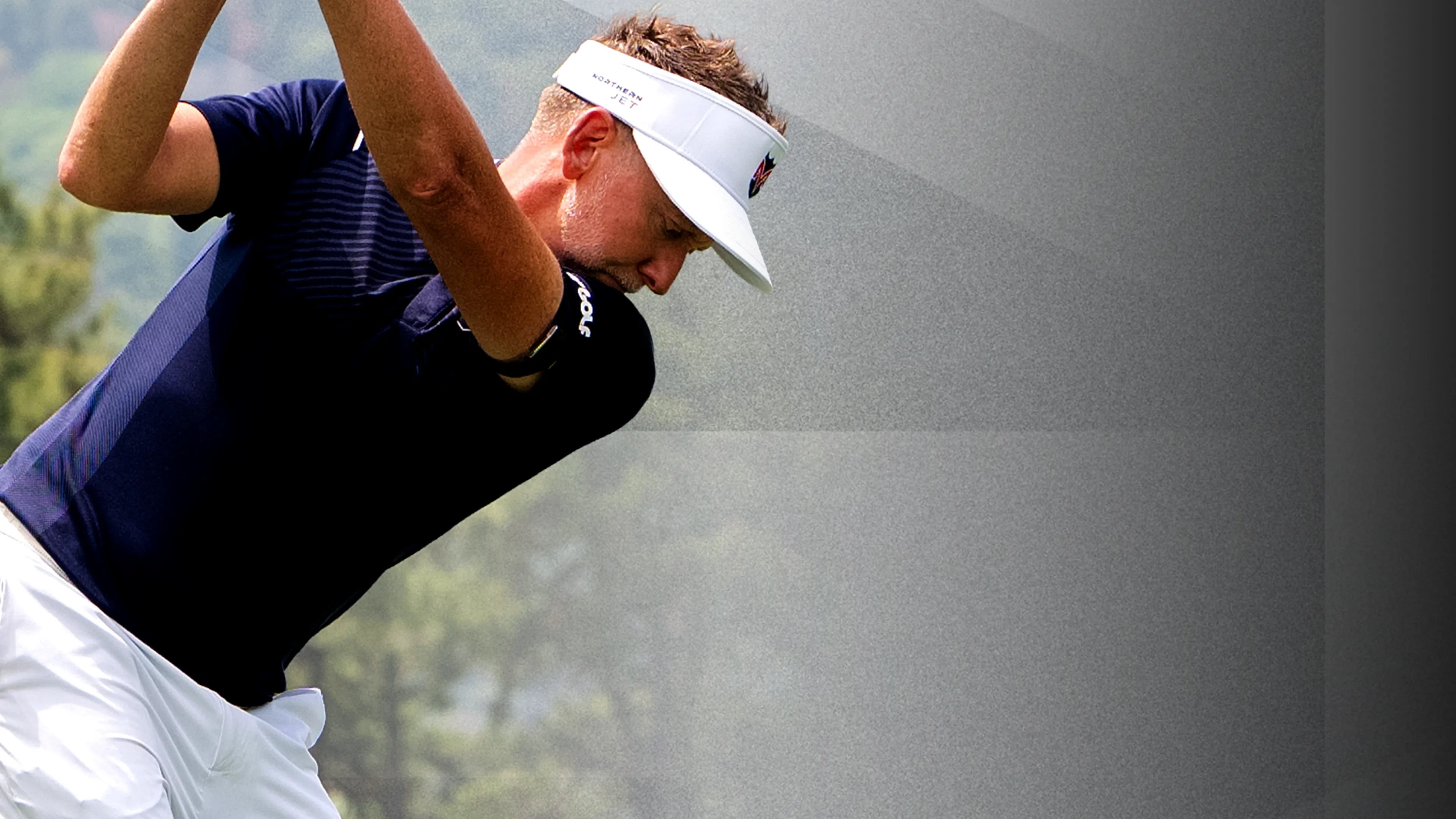 Golfer in a navy shirt and white visor swings a club against a blurred outdoor background.