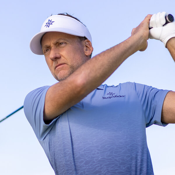 Ian Poulter in a blue golf shirt and cap with a logo, looking to the side against a clear sky background