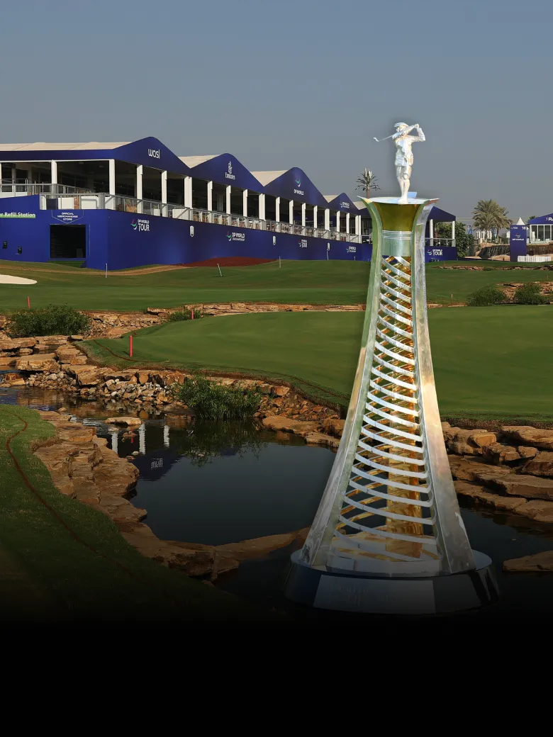A modern golf course with a tall, sculptural trophy in the foreground, surrounded by green lawns and blue tournament structures.