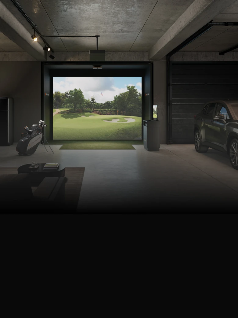 Indoor golf simulator in a modern garage with a golf bag, a car, and a large screen displaying a golf course under bright lighting.