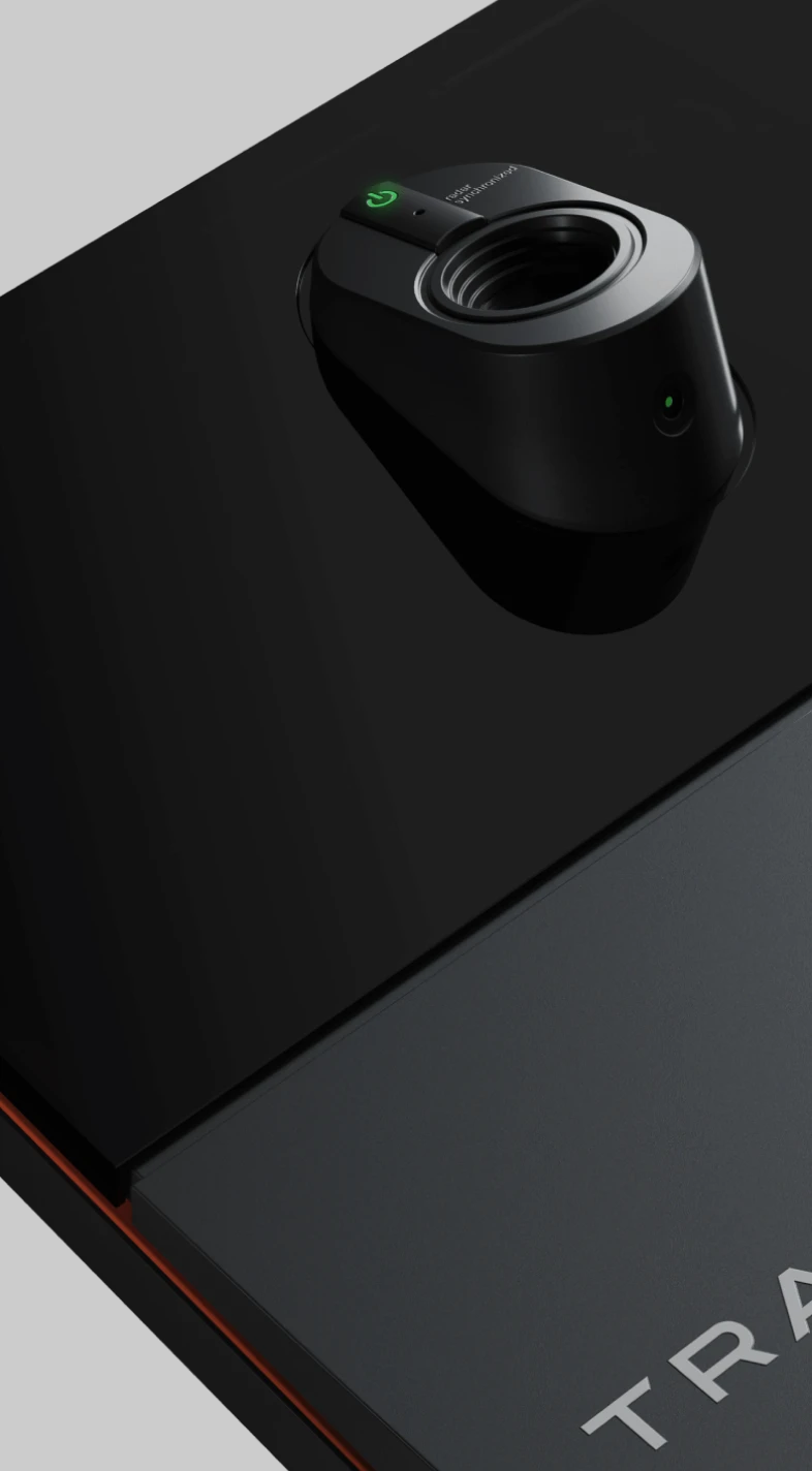 Close-up of a sleek, modern device with a circular lens and green indicator light on a black surface, featuring the word "TRA" partially visible.