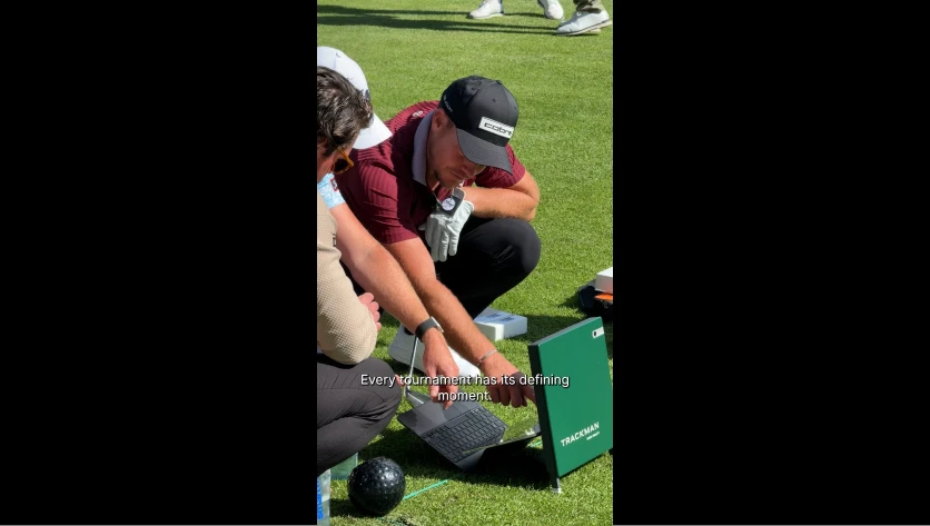 Two golfers crouch on the grass examining a device. Caption reads, "Every tournament has its defining moment."