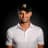 Smiling man in a white polo shirt and black cap with a logo, set against a dark background.