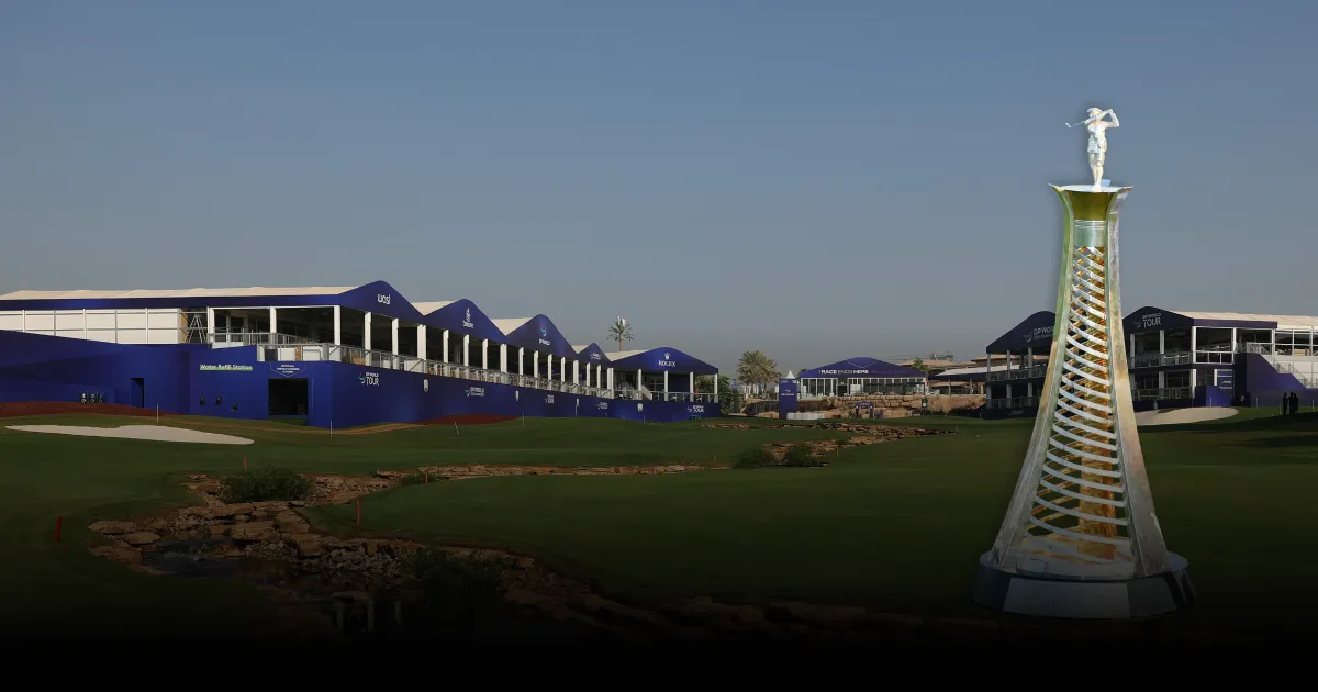 Golf course with a tall, spiral statue in the foreground. Blue-roofed buildings line the background under a clear sky.