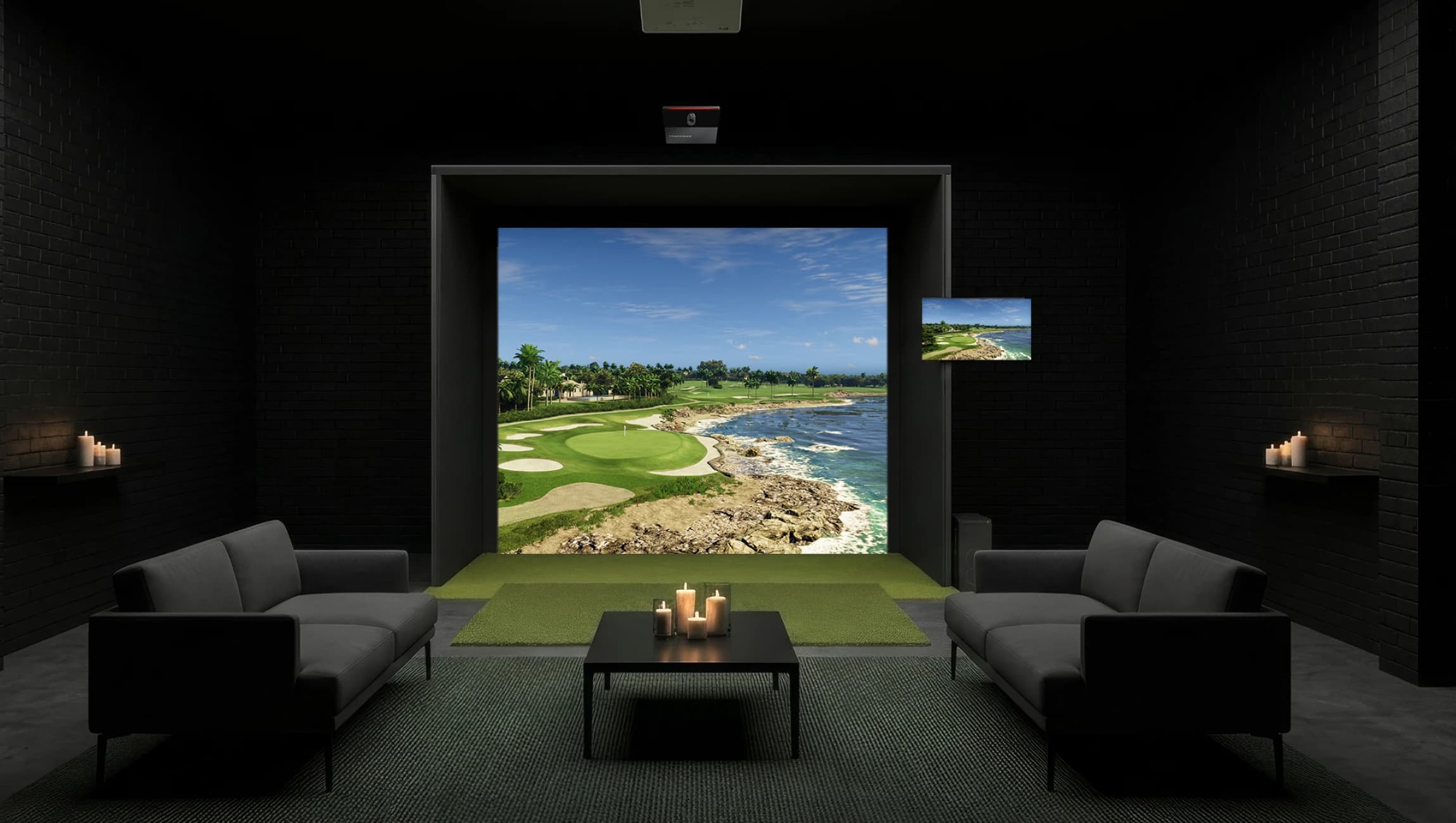 Modern golf simulator room with a large screen displaying a coastal golf course, candles on shelves, and grey sofas on a carpeted floor.