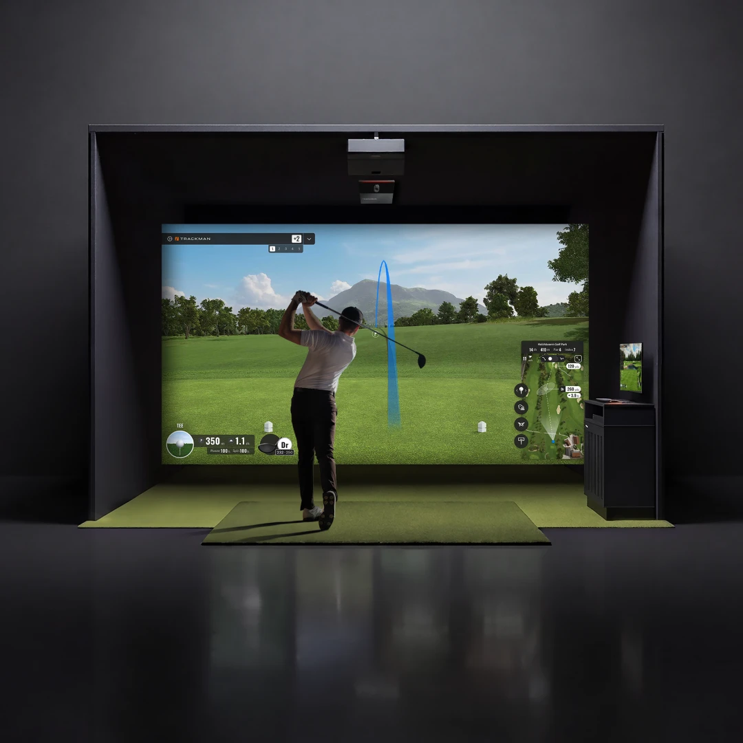 A person is playing golf in an indoor simulator, swinging a club on a virtual course displayed on a large screen.