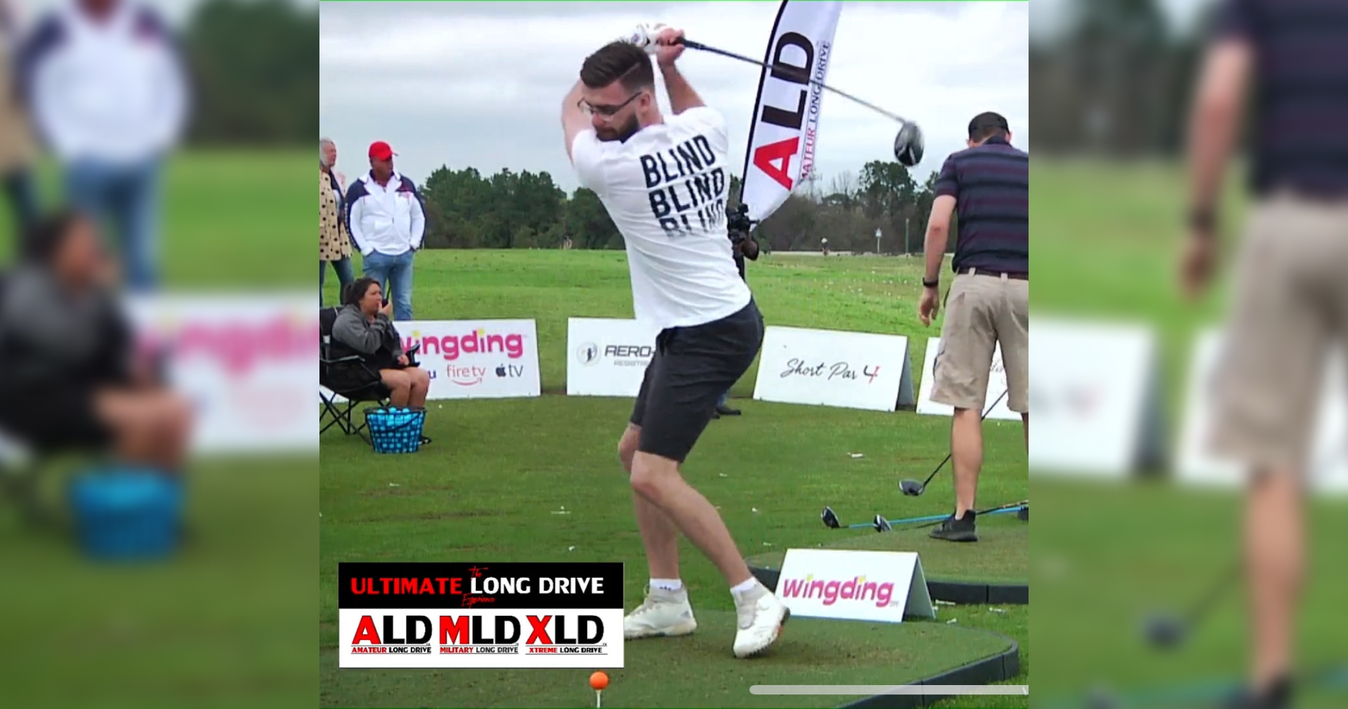 Trackman A man in a "Blind Drive" T-shirt swings a golf club on a grassy field during a long drive competition.