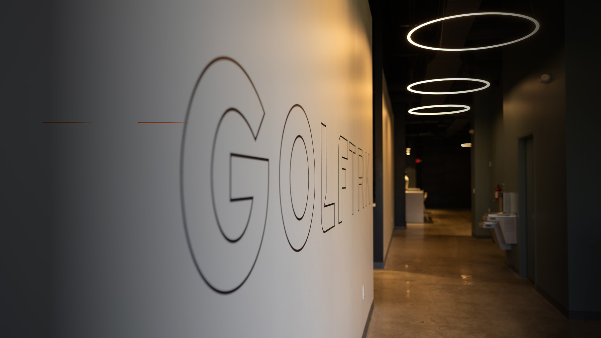 Hallway with the word "GOLF" on the wall, circular ceiling lights, and a distant reception desk in a modern interior.