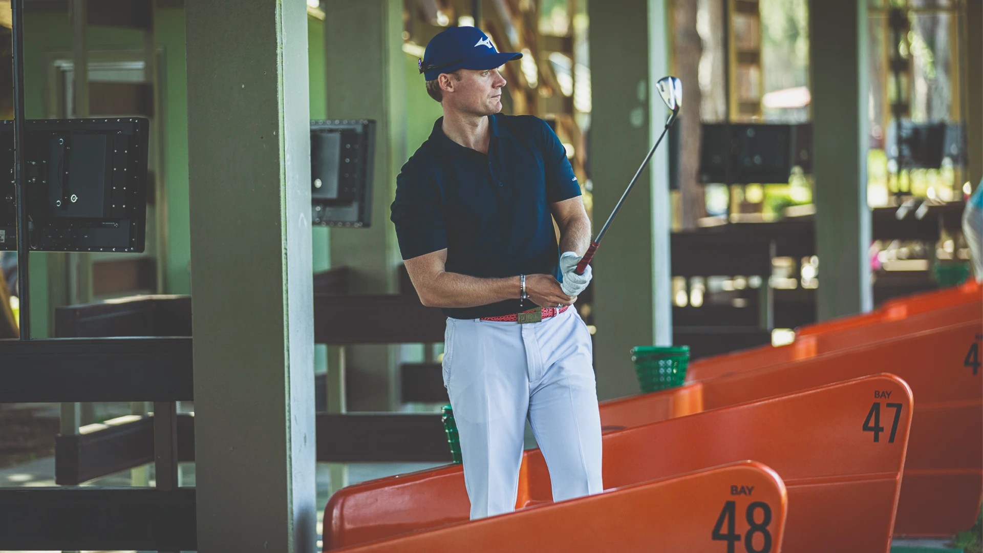 Golfer in blue cap and shirt practicing at a driving range, holding a club near bays numbered 47 and 48.