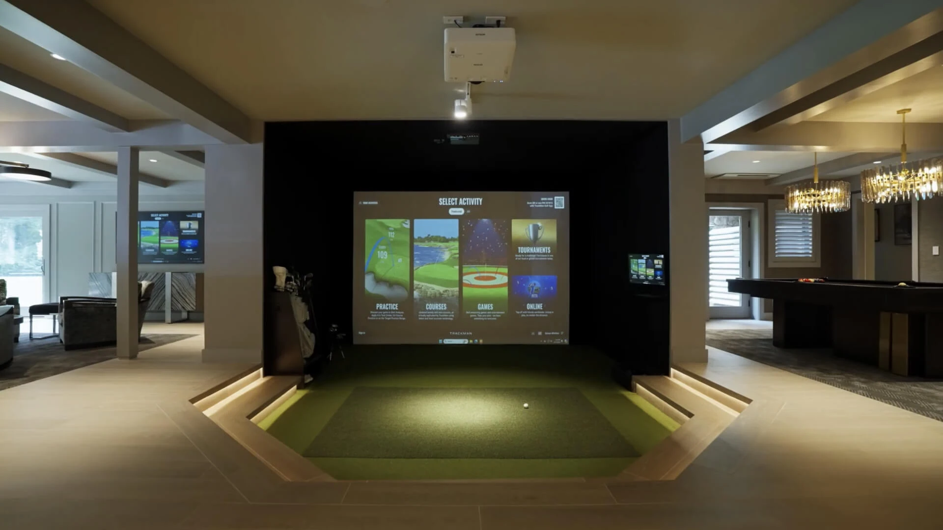 Indoor golf simulator setup in a modern room with large screen, projector, and golf equipment. Elegant decor with a pool table in the background.