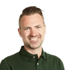 Smiling man with short hair wearing a dark green collared shirt, against a white background.