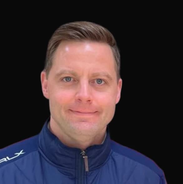 Smiling man in a blue jacket against a black background.