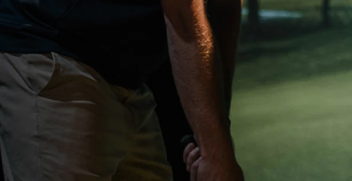 Person holding a golf club, standing on a grassy area, wearing beige pants.