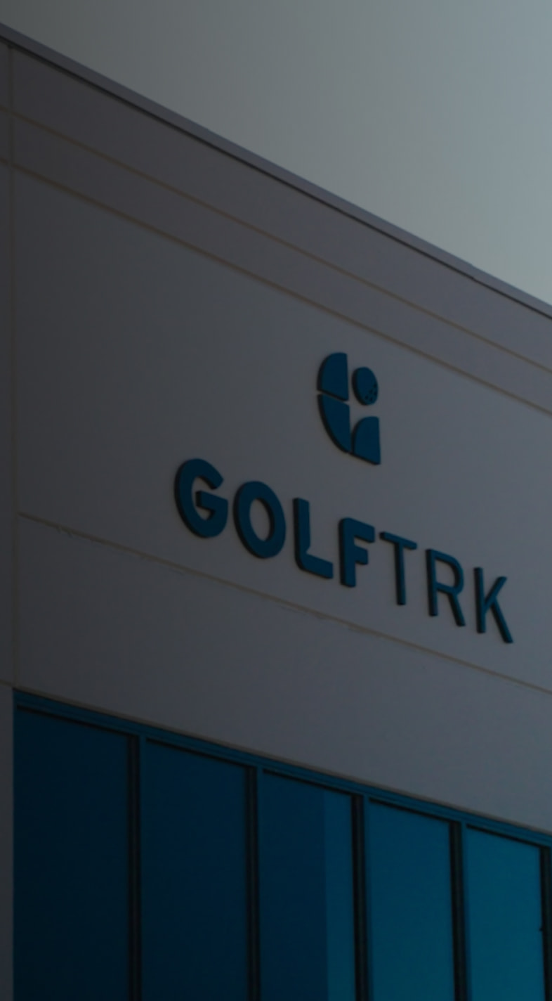 Building facade with "GOLFTRK" signage and a logo above, featuring blue-tinted windows and a modern architectural design.